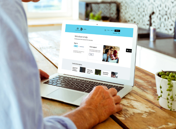 A man typing on a laptop that is showing the official myGov homepage