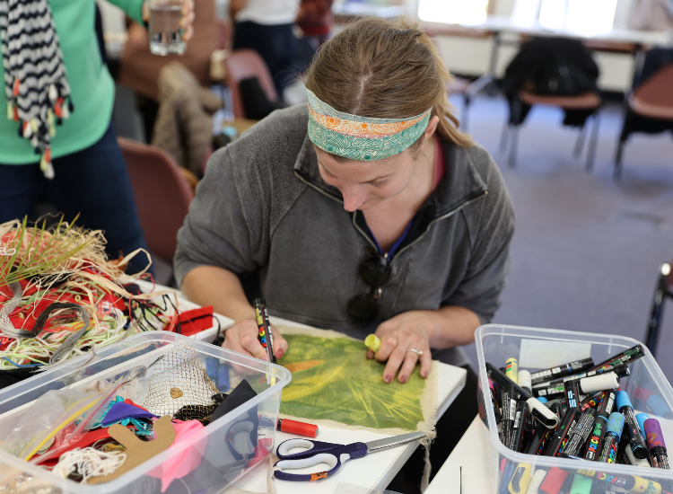 A woman sitting at a table drawing and surrounded by craft materials