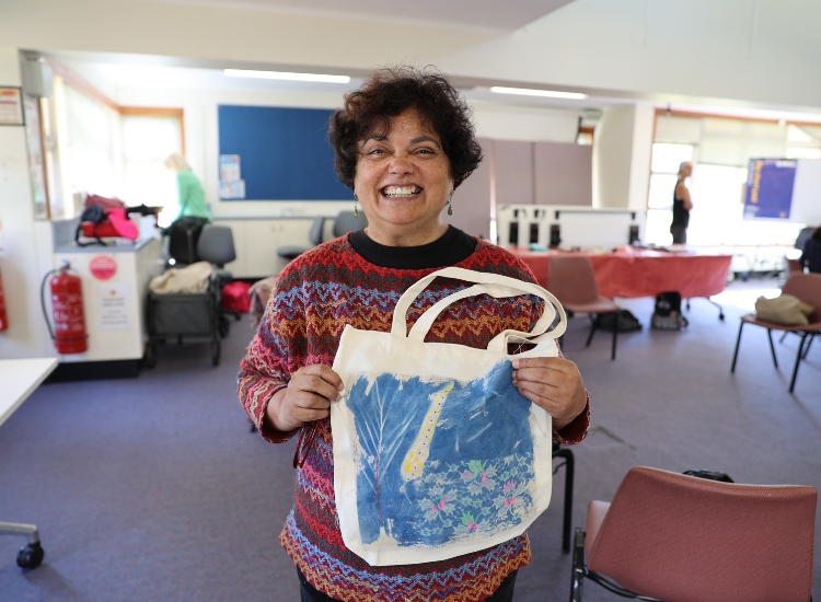 A woman smiling and holding a tote bag decorated with a blue artwork
