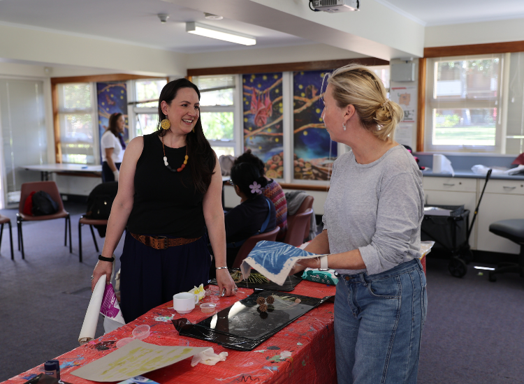 Two women standing over a table smiling at each other, one of them holding a blue artwork
