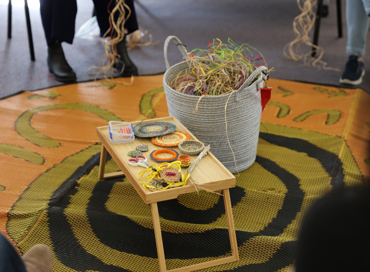 A small table with colourful woven circles and a basket with more weaving string