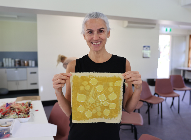 A woman holding a yellow artwork and smiling