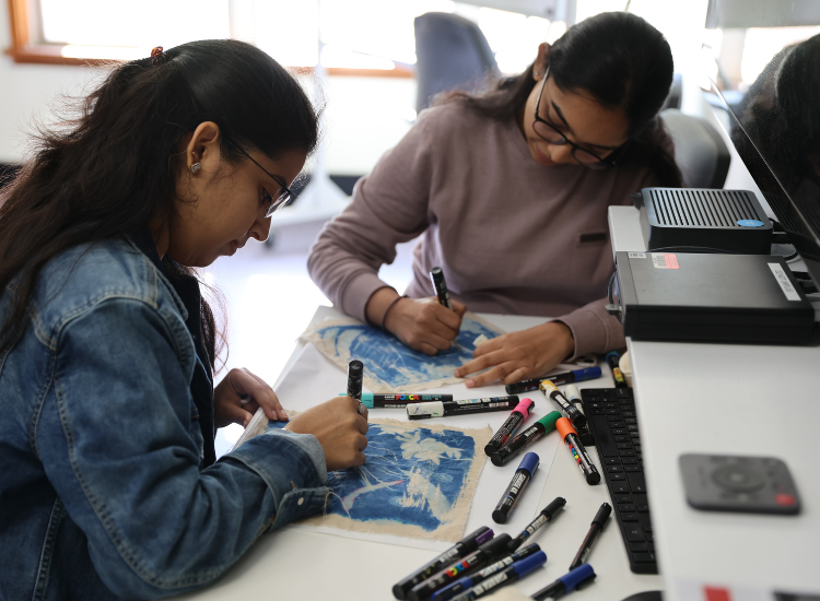 Two women sitting at a table drawing