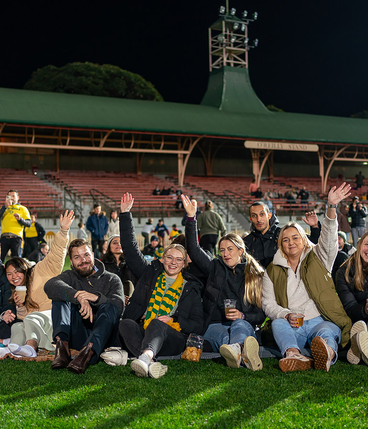 Four people sitting on the grass at North Sydney Oval smiling.
