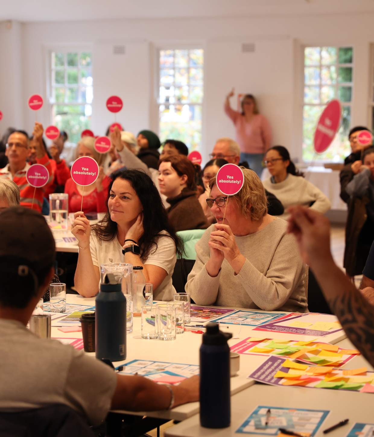 Two women seated, holding small pink signs that say yes absolutely