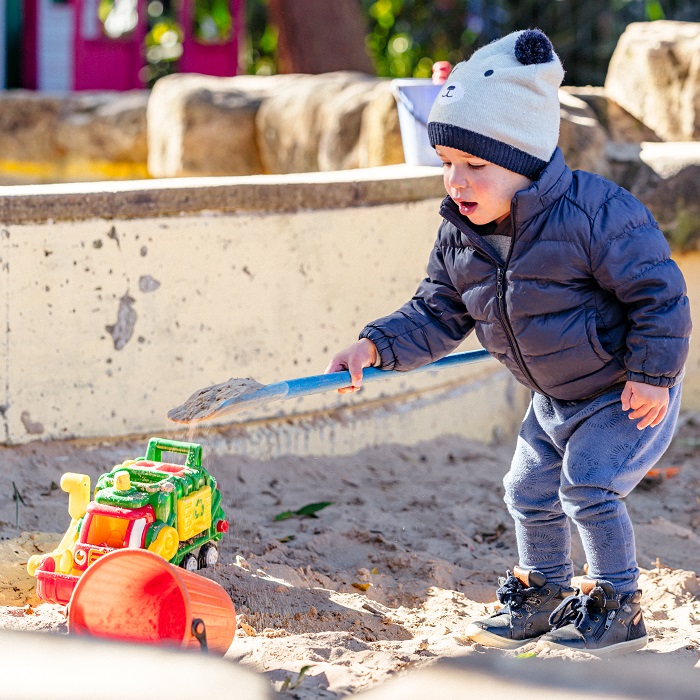 A child playing in a sandpit with a spade and toy truck
