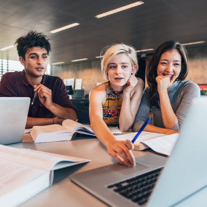 3 university students studying at a table looking at a laptop.