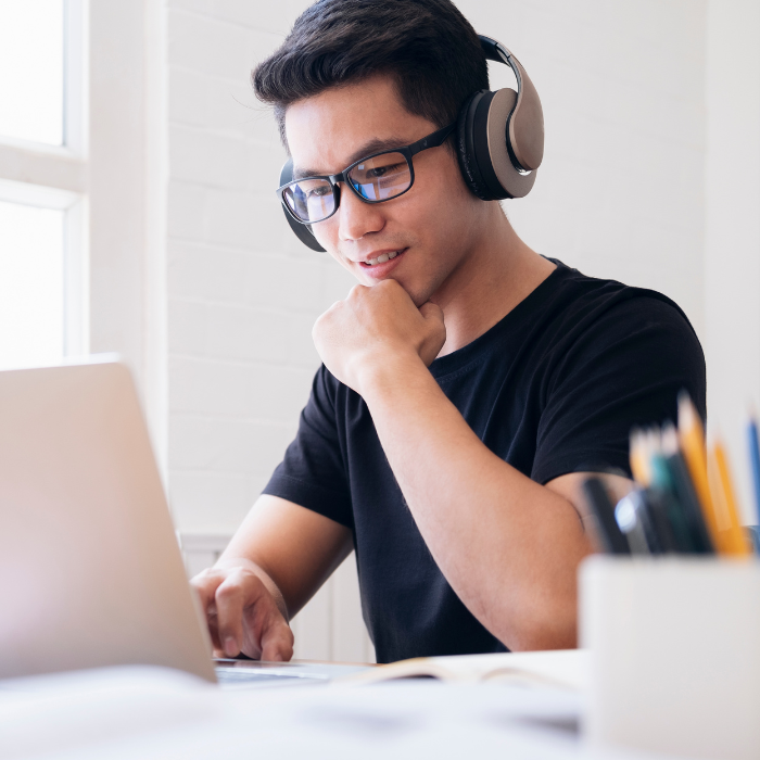 A young man wearing headphones and smiling while using laptop.