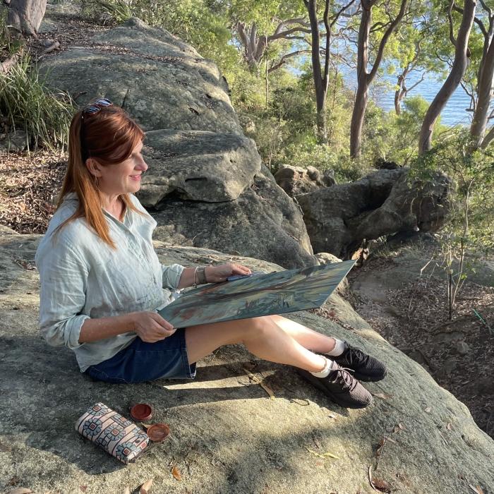 woman sitting on a rock outside drawing