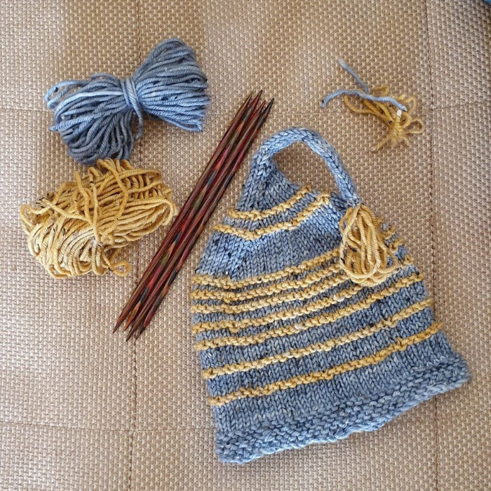 balls of yarn, knitting needles and hand knitted beanie on a hessian  background