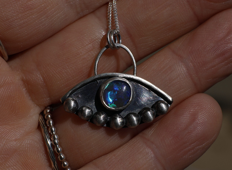 womans hands wearing various rings and holding a dandelion flower