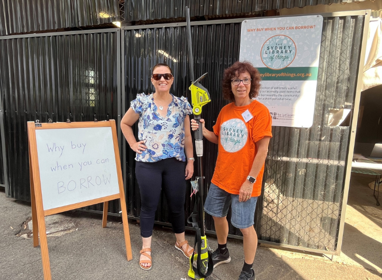 Two people posing beside a sign that says 'Why buy when you can borrow?'