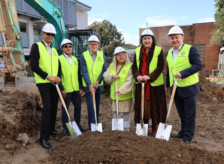 A group of six people wearing hard hats and high-vis vests holding shovels on a construction site