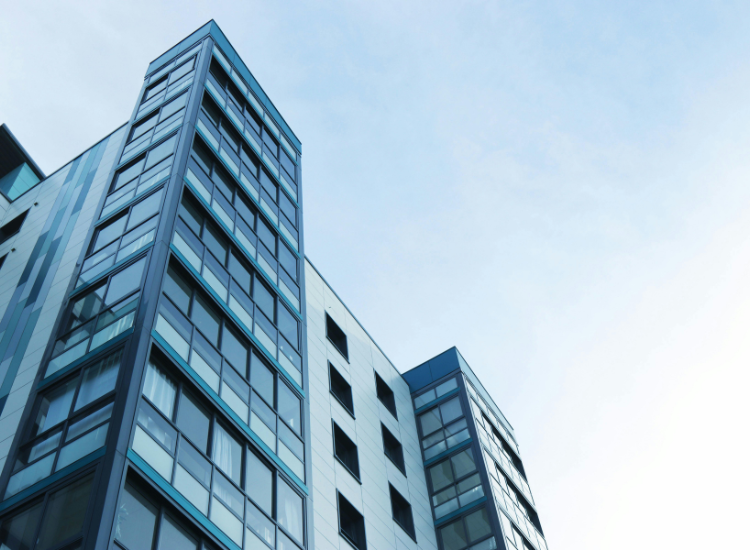 A low-angle shot of a grey blue apartment building against blue sky