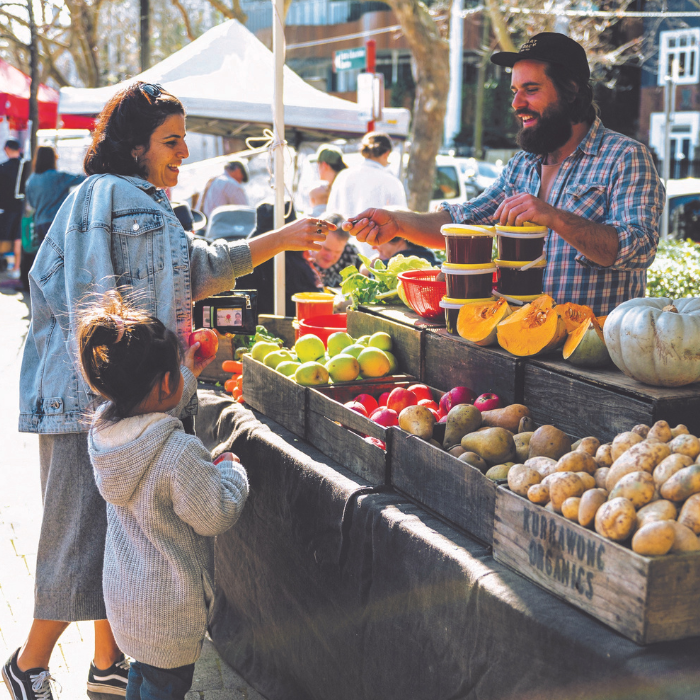 A woman and child paying a man at a produce stall at a market