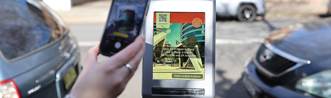 parking meter machine on street with a hand holding a phone towards the meter