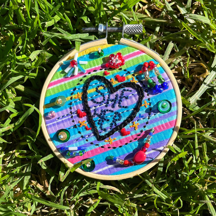 Image of a fabric pronoun pin stitch holder lying on top of grass