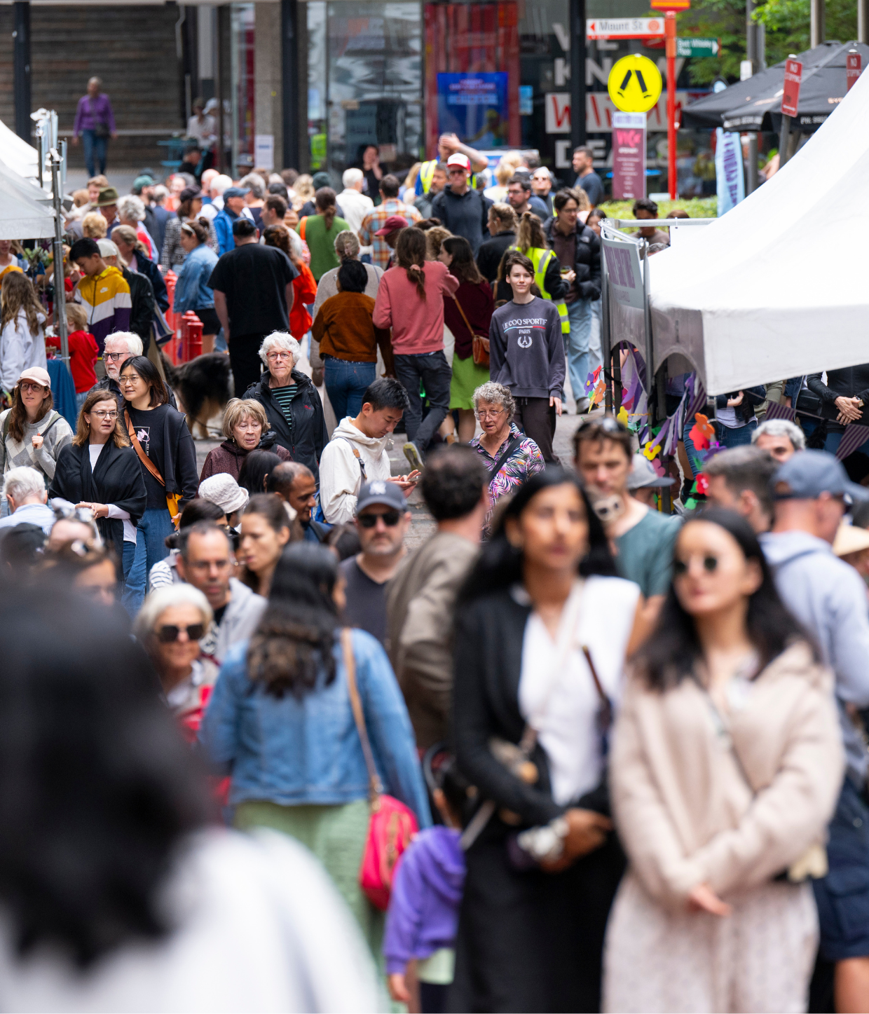 Crowd of people walking along lane in North Sydney with market stalls beside.