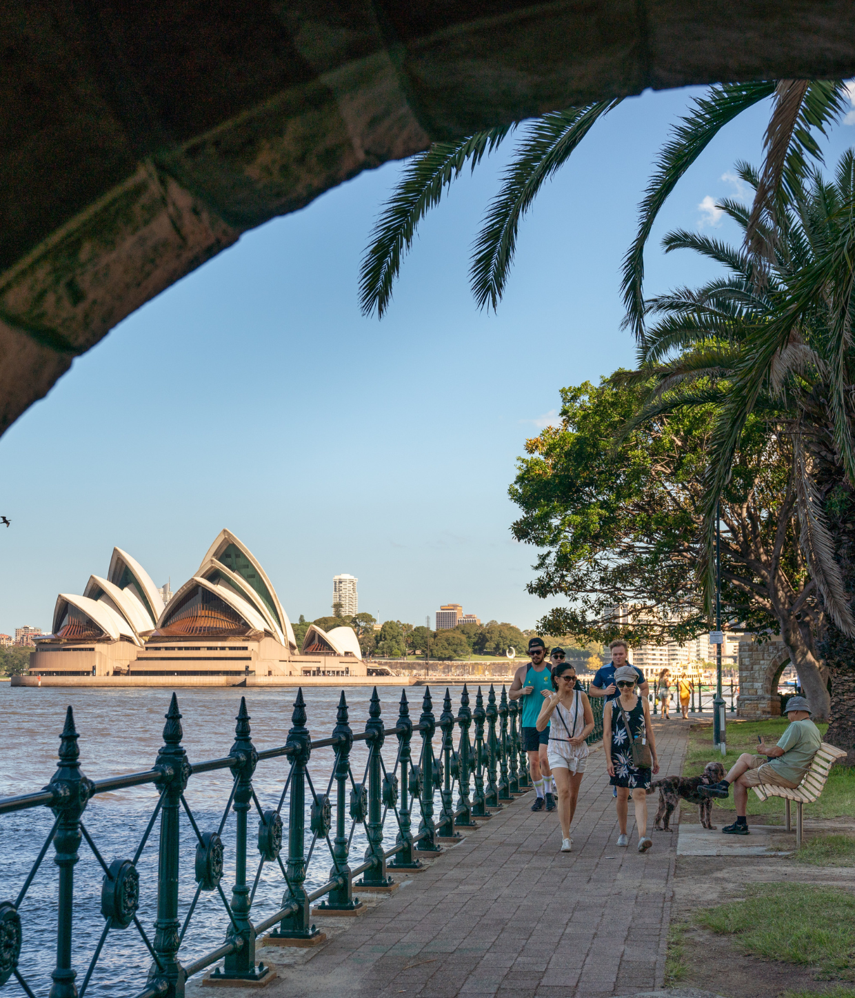 people walking along path of sydney harbour foreshore. The opera house is in the background