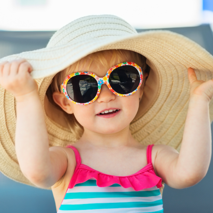 A little girl wearing sunglasses and a large sun hat