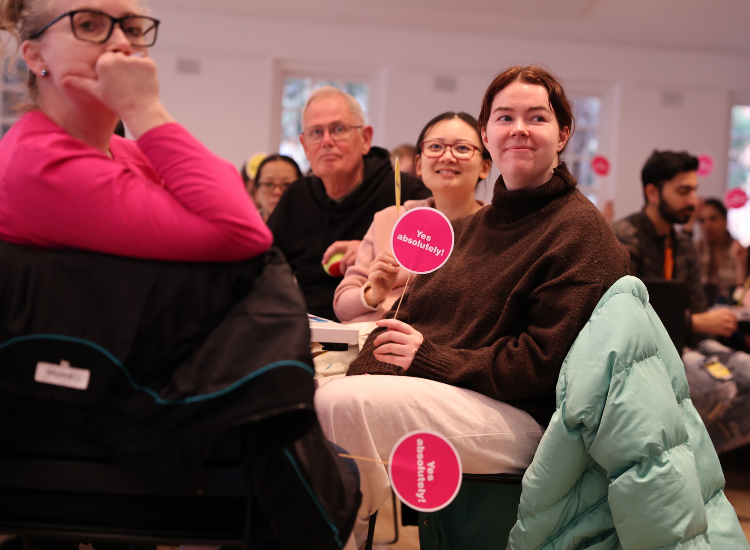 3 people seated at a table turned to look at a speaker 