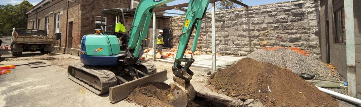 worker in high vis driving an earth mover digging a hole