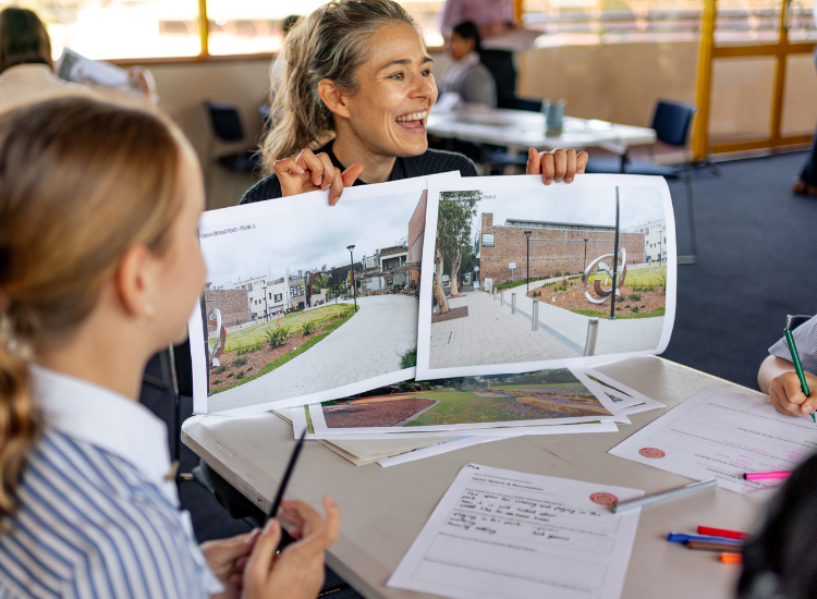 smiling teacher holding images of a park up students