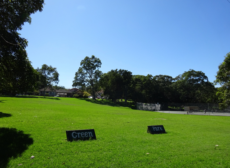 Green grass with a sign displaying 'Green Park' with trees in the background and blue sky above