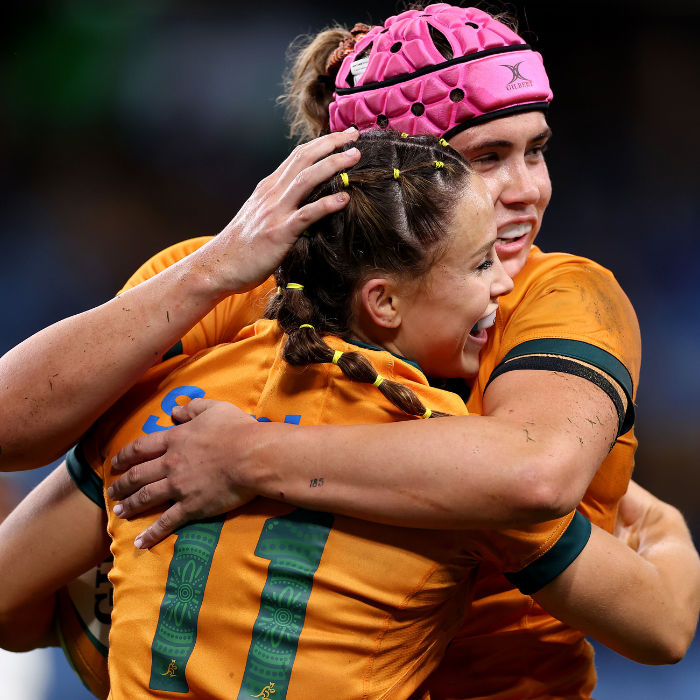 Two Wallaroos players hugging in celebration and smiling