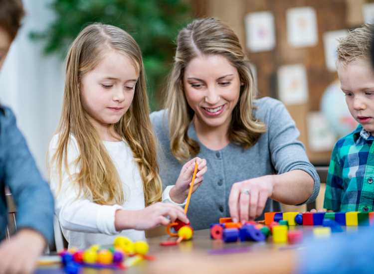 Kids and childcare provider playing with blocks on a tbale