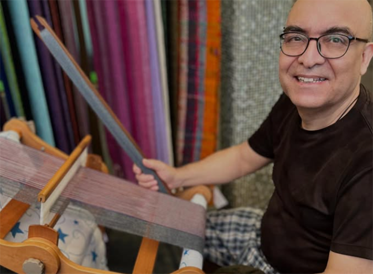 man seated in front of weaving equipment