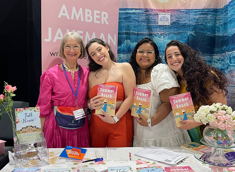 four women standing smiling and holding books