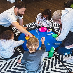 A group of children and carers sitting on the ground playing with colourful toys.