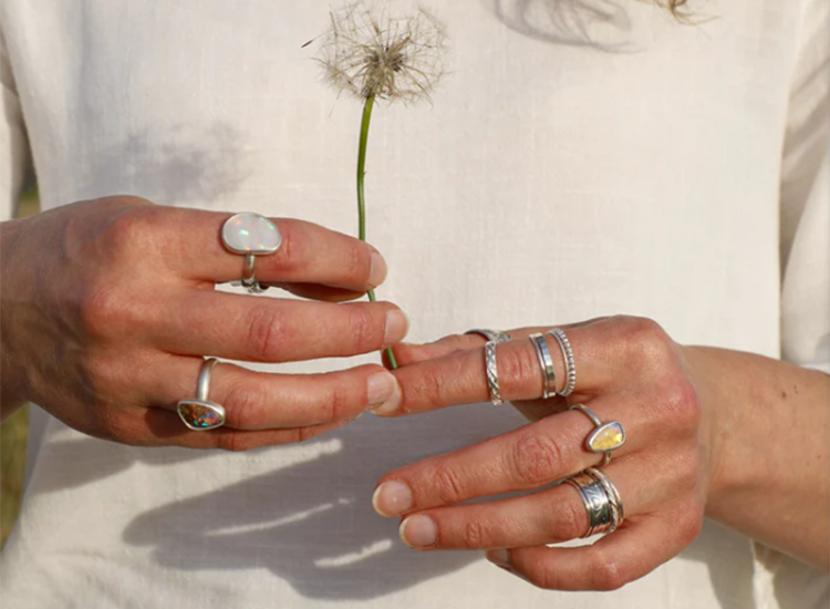 womans hands wearing various rings and holding a dandelion flower