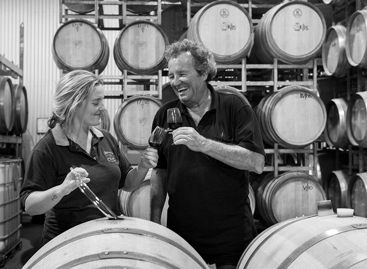 woman and man standing with wine barrels behind them smiling