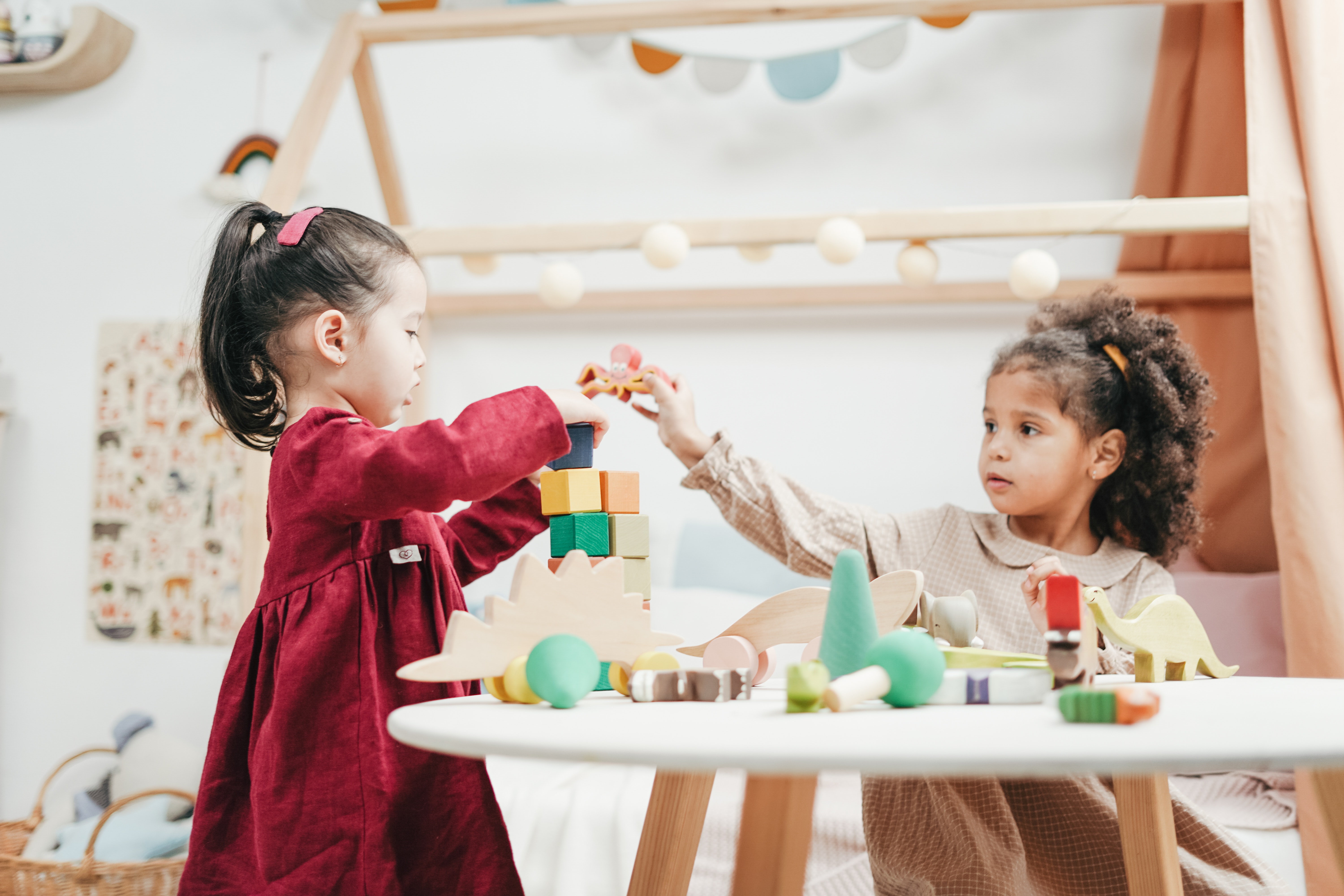 two young girls with dark hair wearing dress, sitting inside playing with blocks