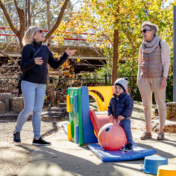 Two women chat while a child plays with toys and play equipment